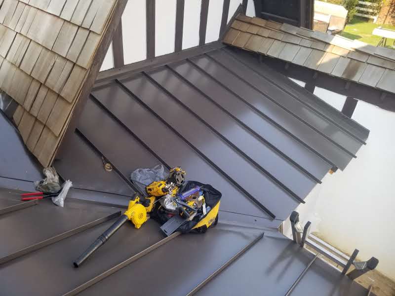 A metal roof with construction tools, including a yellow drill and blower, spread on it near wooden shingles.