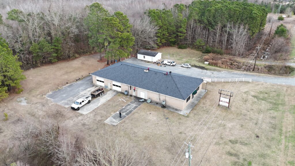 Aerial view of a single-story building with vehicles parked outside, surrounded by trees and an open field.