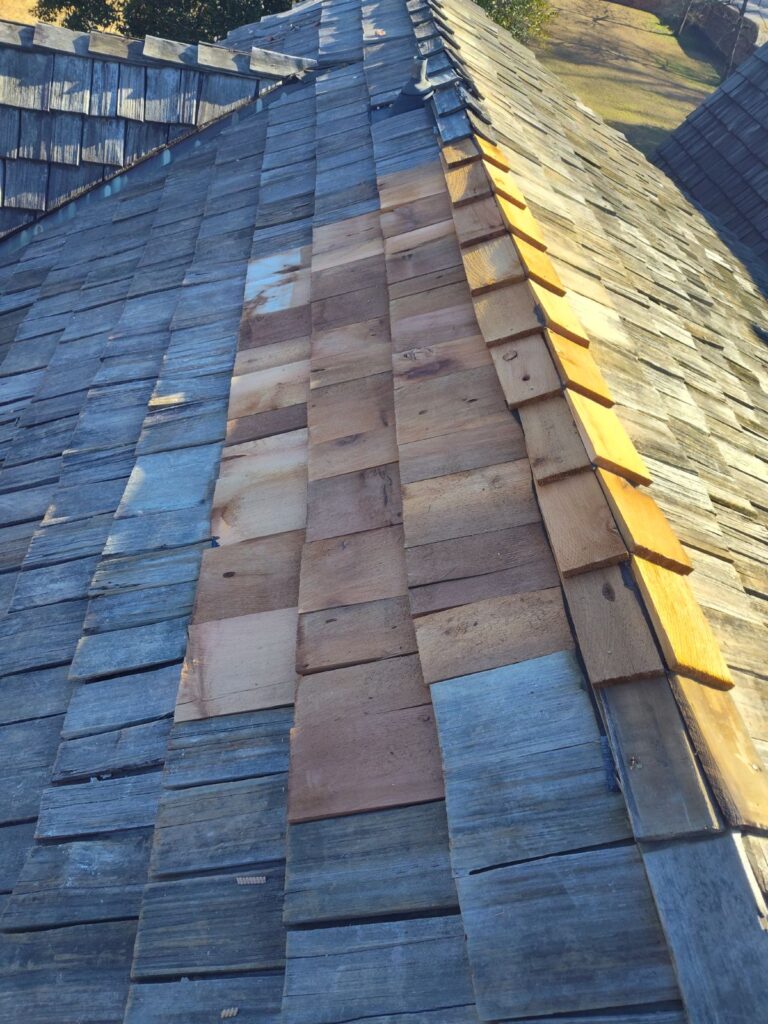 New wooden shingles installed in a vertical strip on an old roof with weathered shingles.